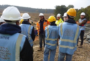 Students in hard hats and hi-viz vests near a wooded area